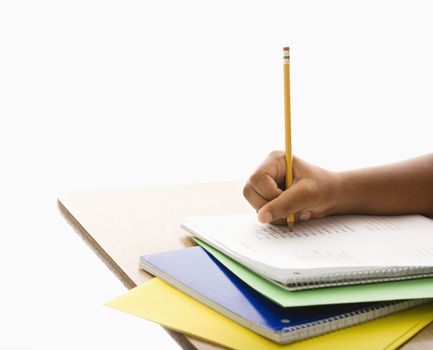 Hand of African American girl at school desk writing in notebook with pencil.