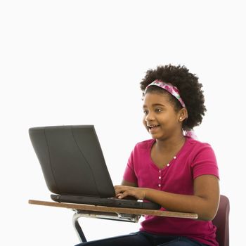 African American girl sitting in school desk typing on laptop computer.