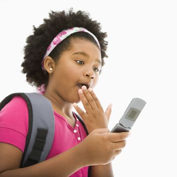 African American girl with backpack looking at cell phone with surprised expression.