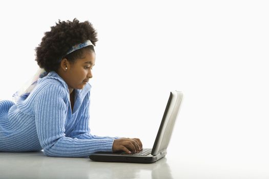 Side view of African American girl lying on floor using laptop.