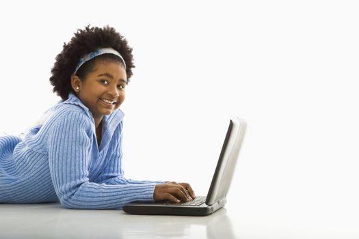 Side view of African American girl lying on floor using laptop and smiling at viewer.