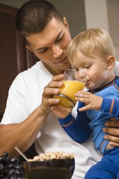 Caucasian man helping toddler son drink juice.