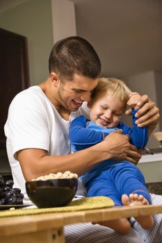Caucasian man tickling toddler son in kitchen.