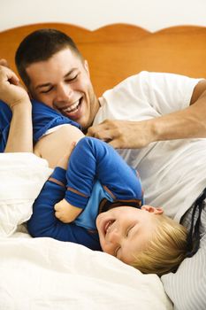 Caucasian toddler boy and father playing and tickling in bed.