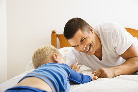 Caucasian toddler boy and father playing in bed.