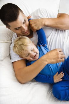 Caucasian toddler boy and father playing and tickling in bed.