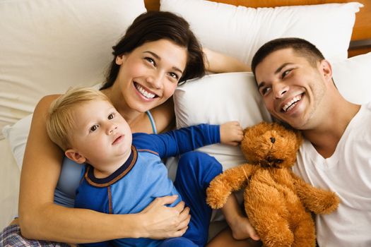 Caucasian parents and toddler son lying in bed smiling.