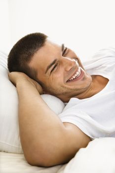 Handsome Caucasian mid adult man lying with hands behind head smiling.