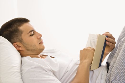 Side view of handsome Caucasian mid adult man lying in bed reading a book.