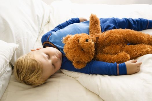 Caucasian toddler boy sleeping in bed with teddy bear.