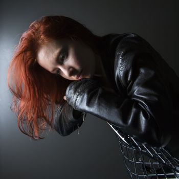 Pretty redhead young woman wearing leather jacket hanging over back of chair.