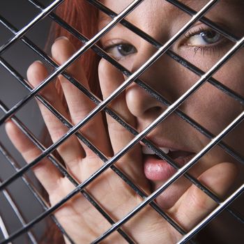 Pretty redhead young woman face and hand behind metal pattern.