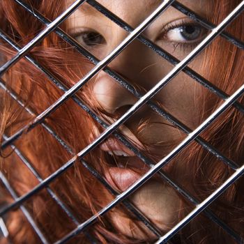 Pretty redhead young woman face behind metal pattern.