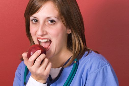 A young nurse bites into a red juicy apple.