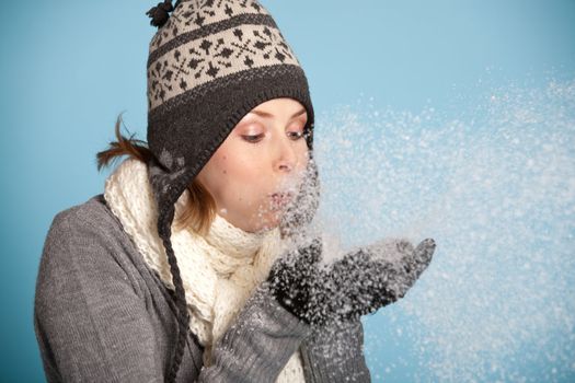 Pretty blond girl with winter clothes blowing snow from her hands
