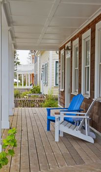 Blue and white adirondack chairs on a the wood porch of a brown shake home
