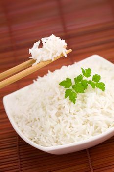 Closeup of rice on chopsticks and a bowl on mat