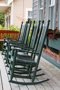 Four green wooden rocking chairs on a porch with partial wood swing
