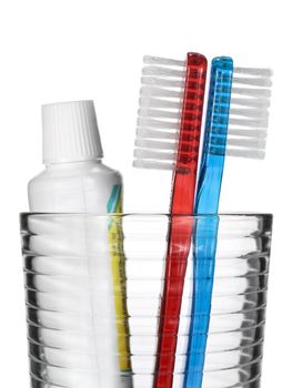 Two toothbrushes and a tube of toothpaste in a glass over white background.