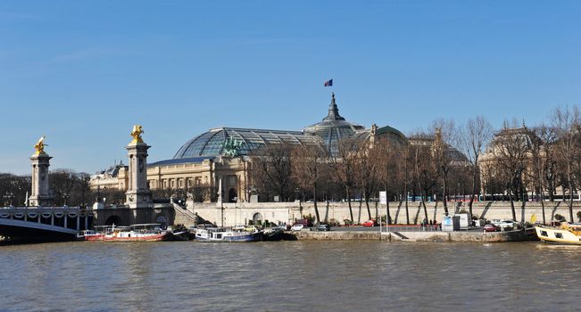 Pont Alexander III arches over the Seine in Paris and the Grand Palais dome in the background.