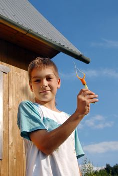 boy showing a carrot by wooden house over blue sky outdoor