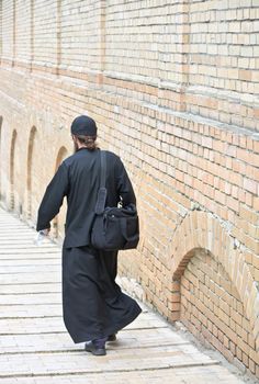 Young ortodox monk in black cassock against the brick monastery wall (the Kiev-Pecherskaya Lavra monastery, Kiev, Ukraine)