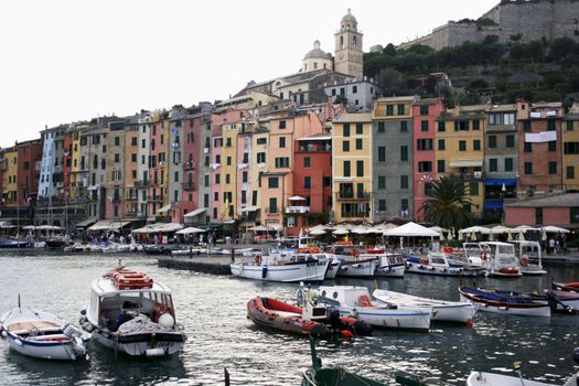 Village of Portovenere in Liguria on Italy's Cinque Terre coast with boats in Mediterranean harbor, view of colorful houses, and sight of Church of St. Pietro on hillside