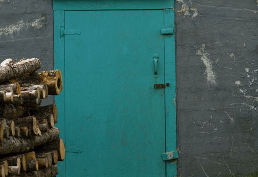 Rural frugality reflected in the turquoise door to an old root cellar fronted by stacked logs of winter firewood