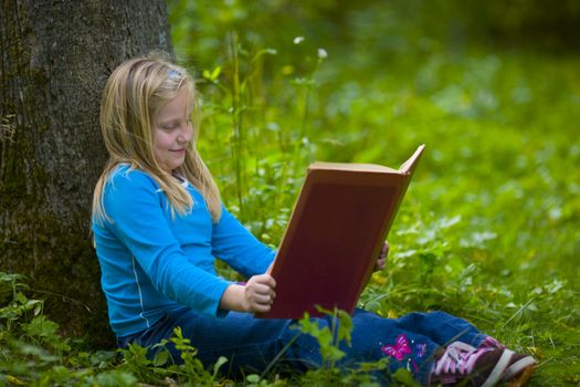 A girl reading under a tree in a green outdoor scene