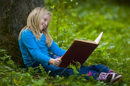 A girl contemplating a good book outdoors under a big tree