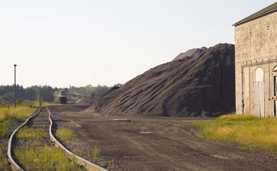 Coal loading in a rail yard on an old train next to massive stacks of coal.