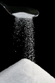 sugar trickling from a silver spoon isolated on black