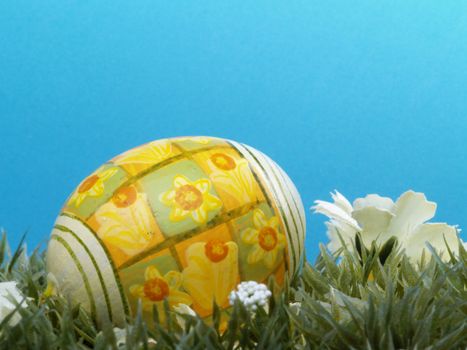 handpainted daffodil design on easter egg, artificial grass and blossoms, shades of blue background