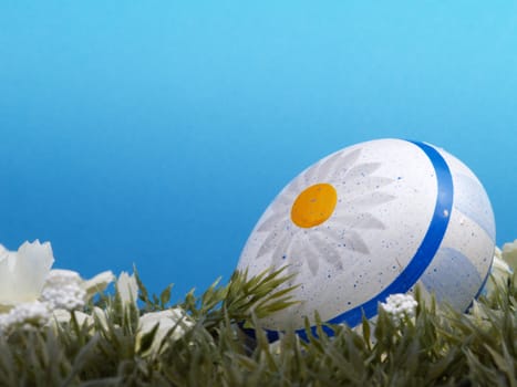 handpainted daisy design on easter egg, artificial grass and blossoms, shades of blue background