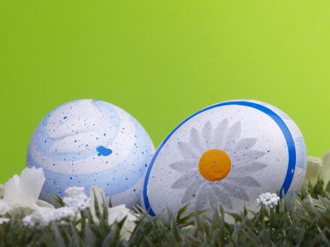 two handpainted easter eggs, artificial grass and blossoms, green background