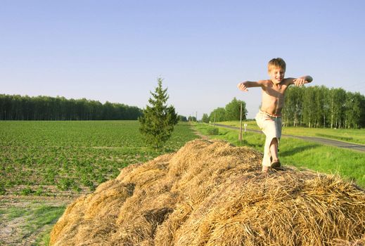 boy jump on a hayrick and throw a straw near road