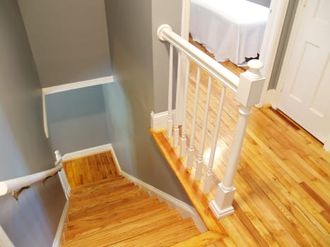 A refinished wooden floor and steps in a stairway. White painted railings and woodwork accent the classic gray walls