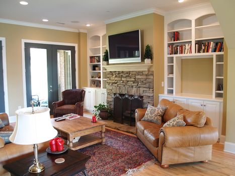 A flat panel lcd or plasma television hangs above the stone fireplace in this modern american luxury home. Leather furniture and bright french doors accent the decor. 