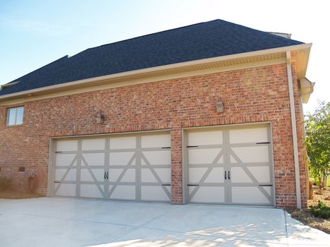 Two garage doors on the side of a modern american brick home with space to park three cars.