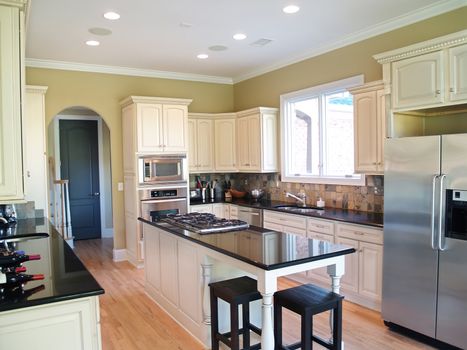 A modern kitchen with white cabinets and black granite countertops. Wine bottles and stainless steel appliances are visible