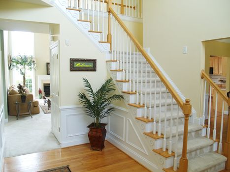 A foyer in a modern american home with a carpeted staircase, a view of the family room, and a prominent Welcome sign (artwork has been replaced with non-copyrighted art)