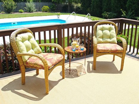 Two comfortable chairs on a patio overlooking a pool in the backyard