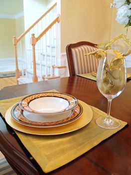 A gold place setting on the dining room table with the staircase in the background