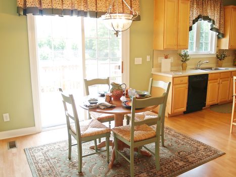 A small breakfast table in front of a bright window. The table is set for a meal, and the kitchen is in the background.