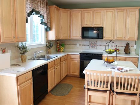 A modern kitchen with maple cabinets and hardwood floors. An island countertop with two barstool chairs make a perfect place for breakfast