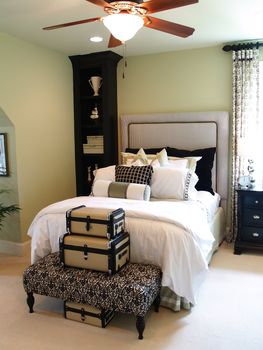A nicely decorated guest bedroom with a collection of suitcases, a ceiling fan and a padded headboard