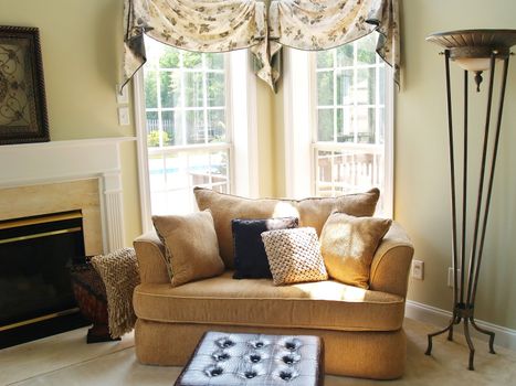 Large chair and footstool brightly lit by the sun streaming in two windows in a luxury home