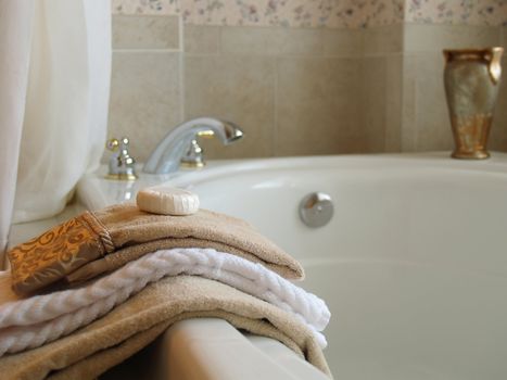 Towels and a bar of soap on the side of a large tub with the faucet and a vase blurred in the bckground