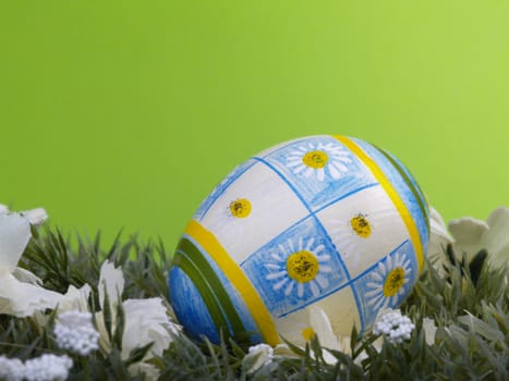 handpainted daisy design on easter egg, artificial grass and blossoms, green background