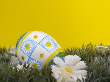 handpainted daisy design on easter egg, artificial grass and blossoms, yellow background